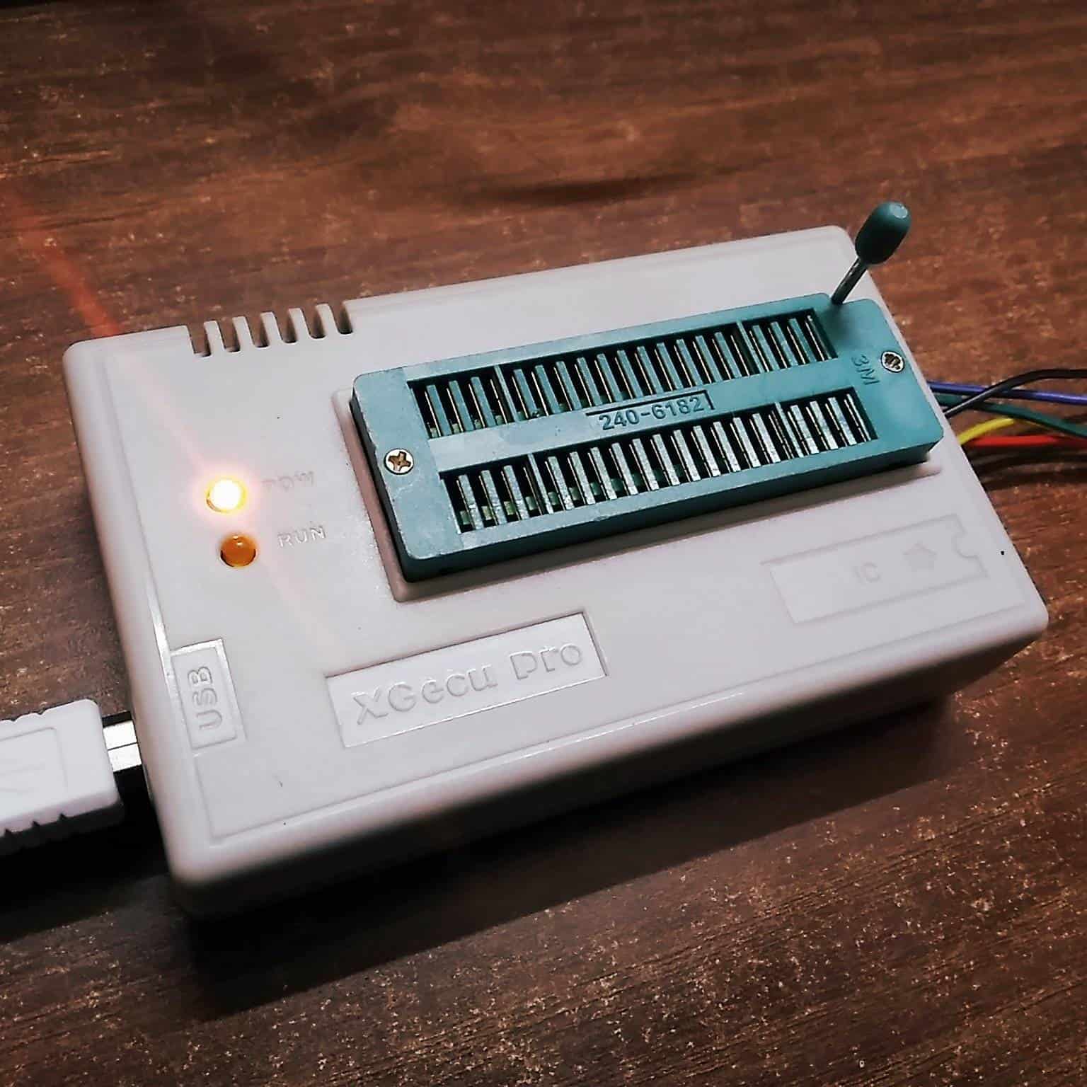 Close-up photo of XGecu Pro TL866II Plus universal programmer with ZIF socket, USB cable connected, PWR LED lit, RUN LED, and ICSP header wires on a wooden desk